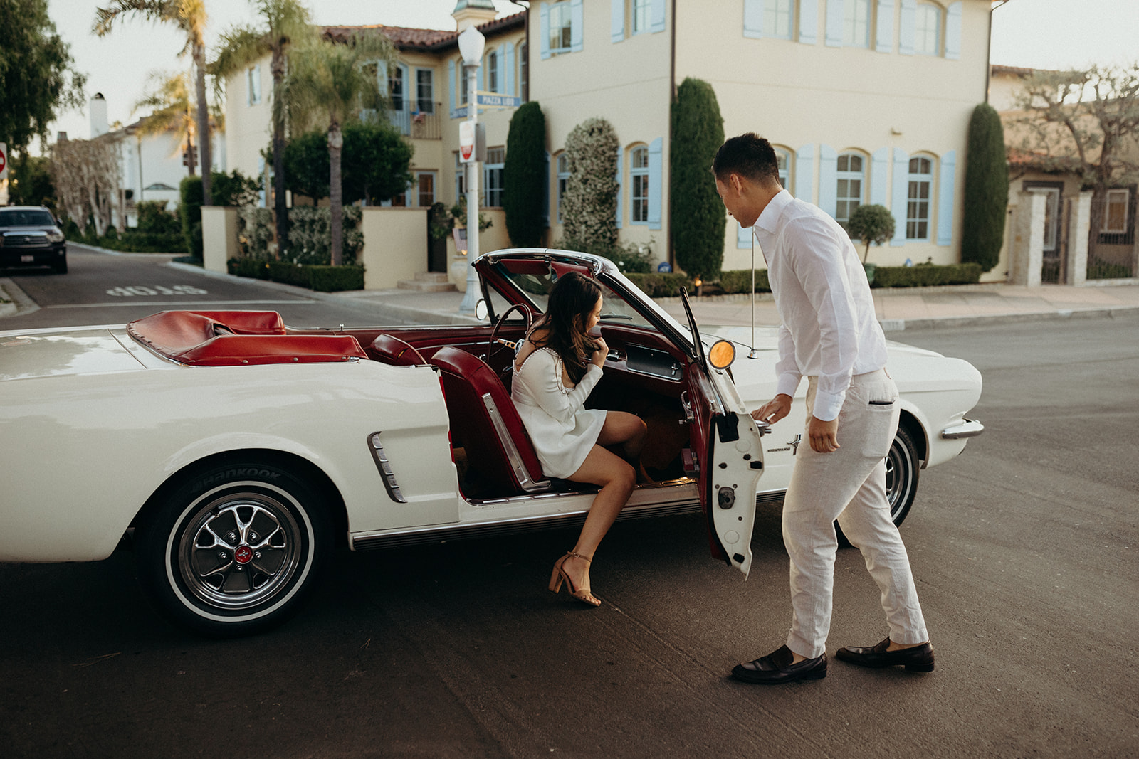 woman getting into a white vintage mustang while man opens door