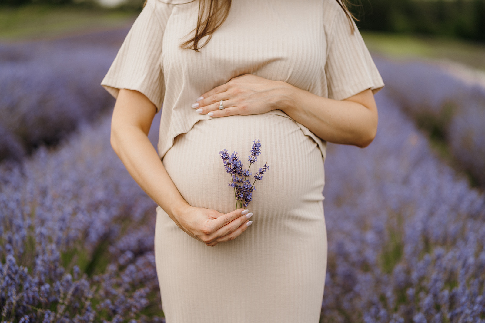 Woman holds a piece of lavender near the bottom of her stomach while resting her other hand on top.