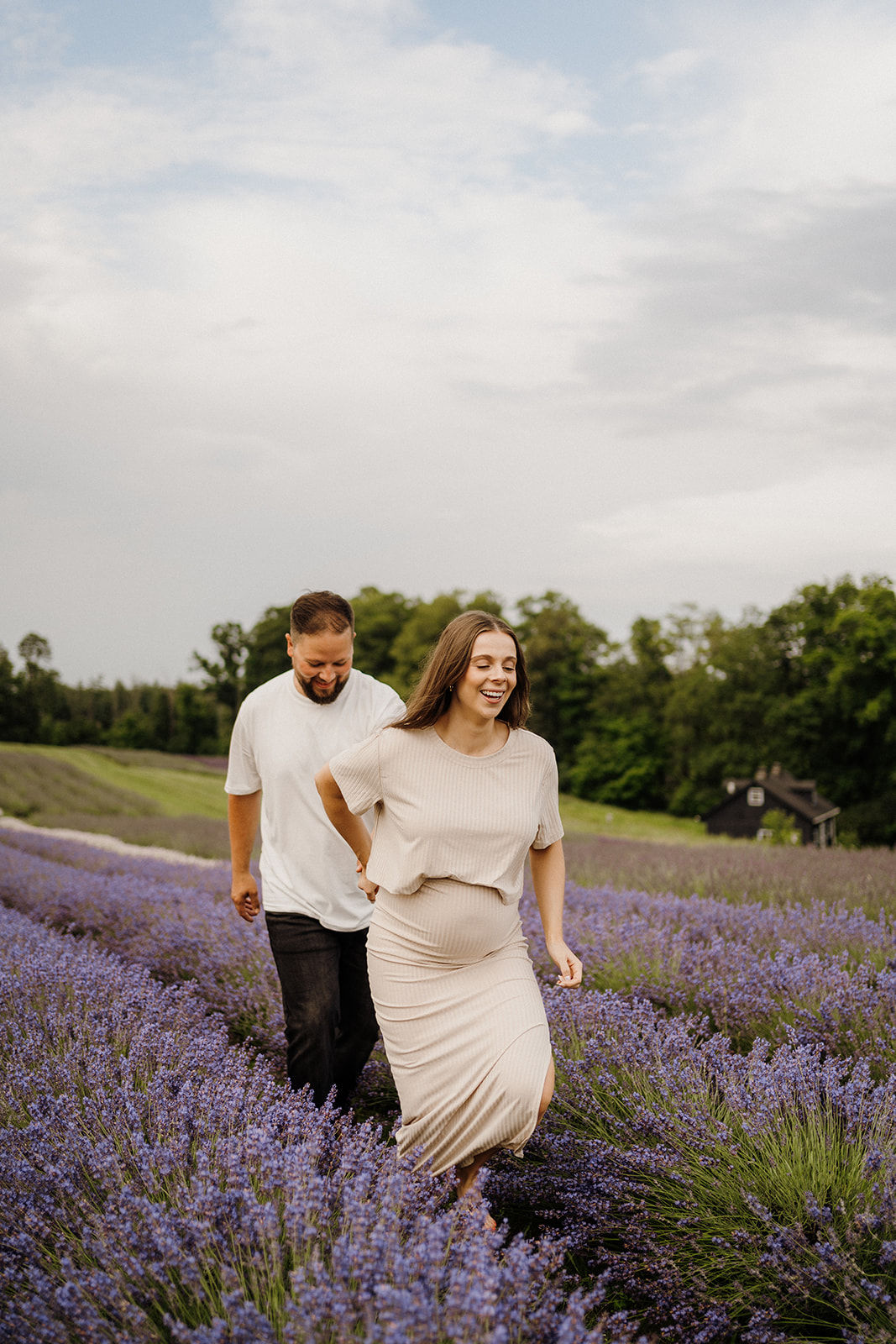 Woman holds the man's hand while walking in front of him in the lavender fields.