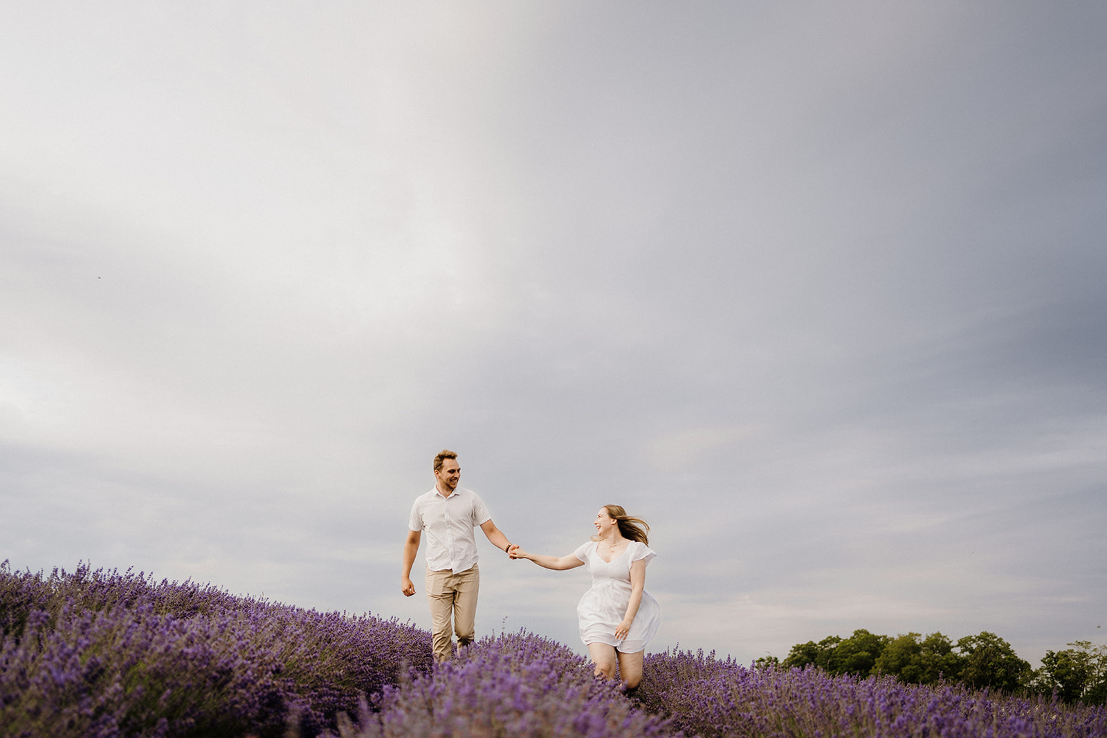 Man and woman holding hands walking down the field of lavender.