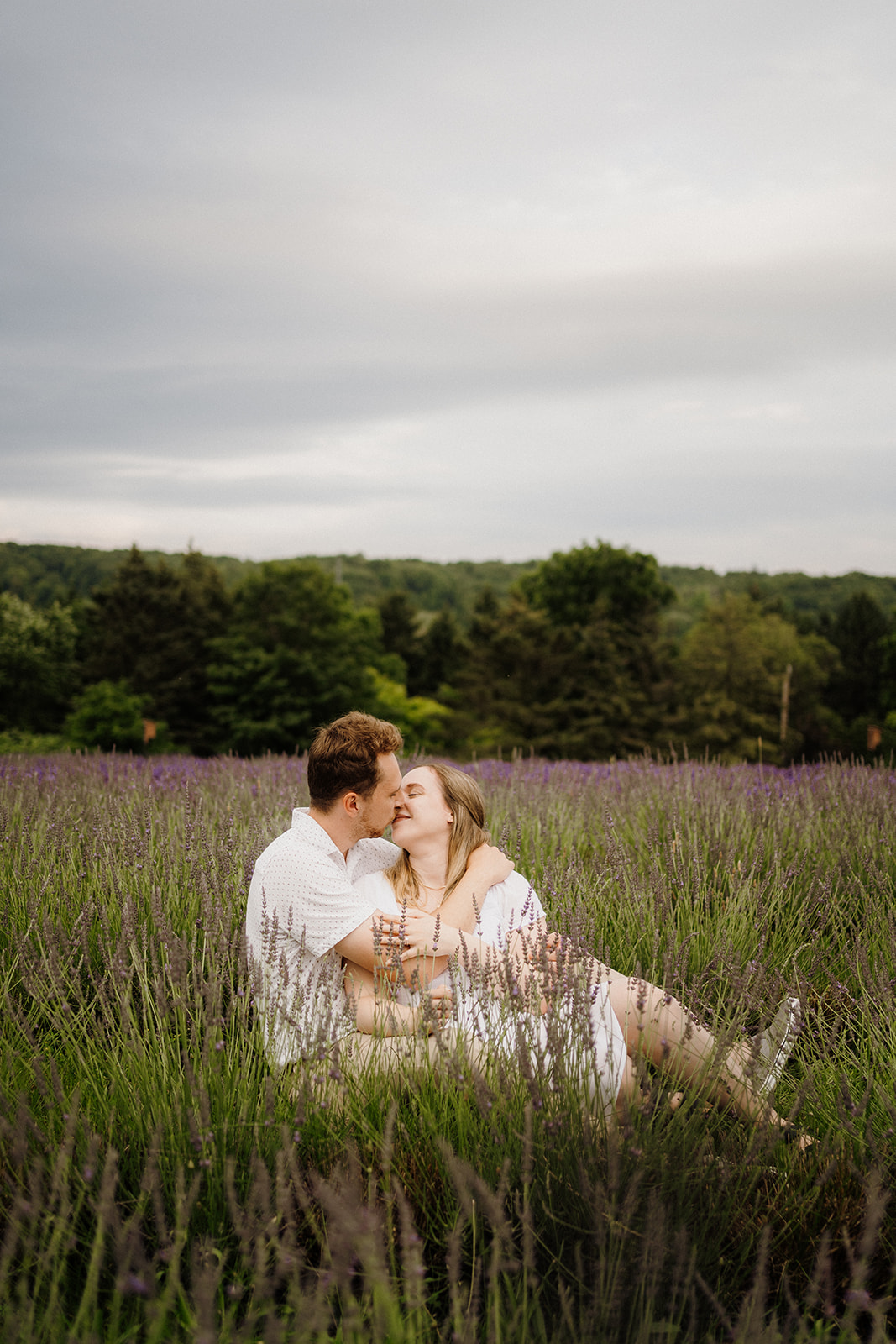 Man and woman touch noses while sitting in the grass.