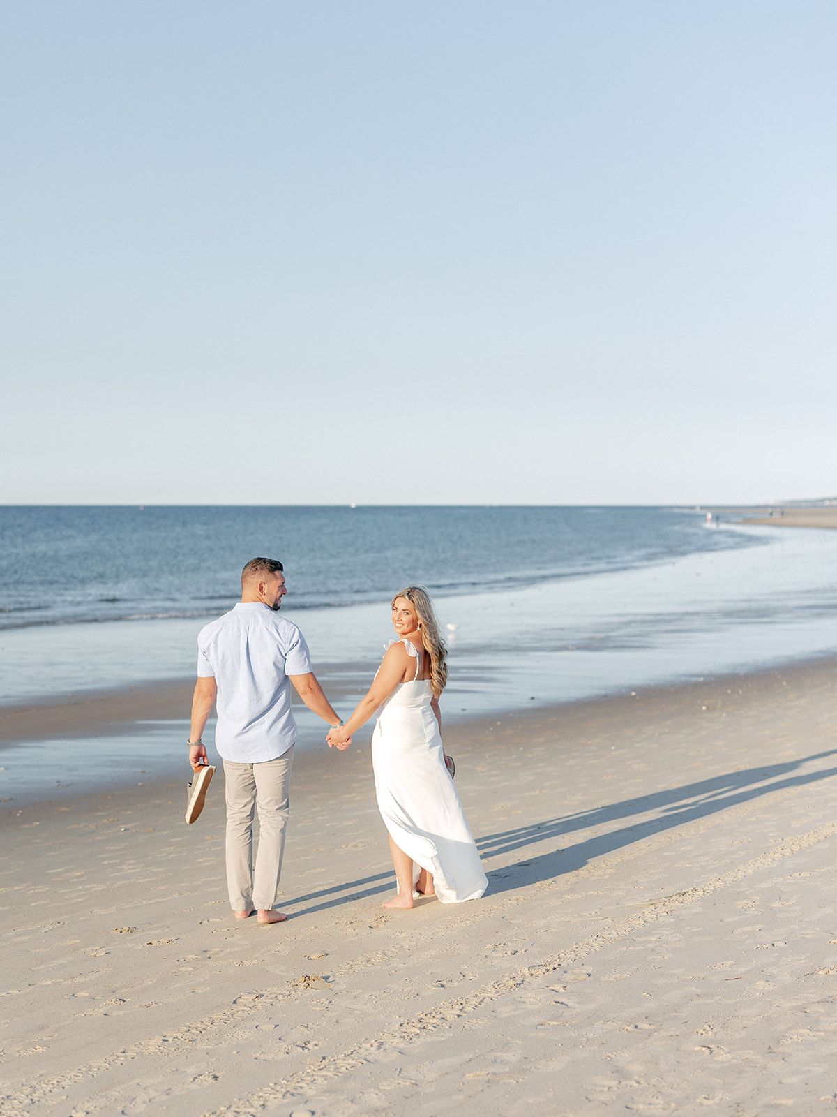 Bride and groom walk along the water at Crane Beach for their engagement session photos.
