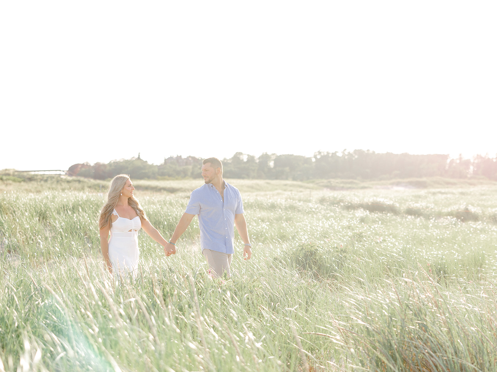 Bride and groom walk through grass on their way to Crane Beach in Ipswich, MA on the North Shore.