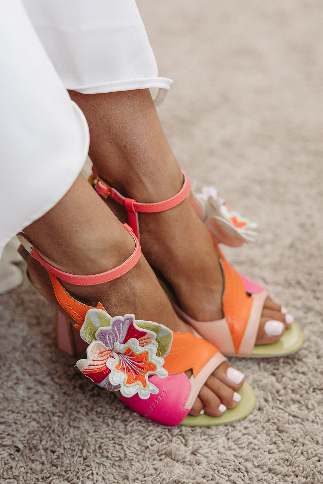 A closeup look at the bright orange and pink floral sandals of the bride. Her white toes peek out of the front.