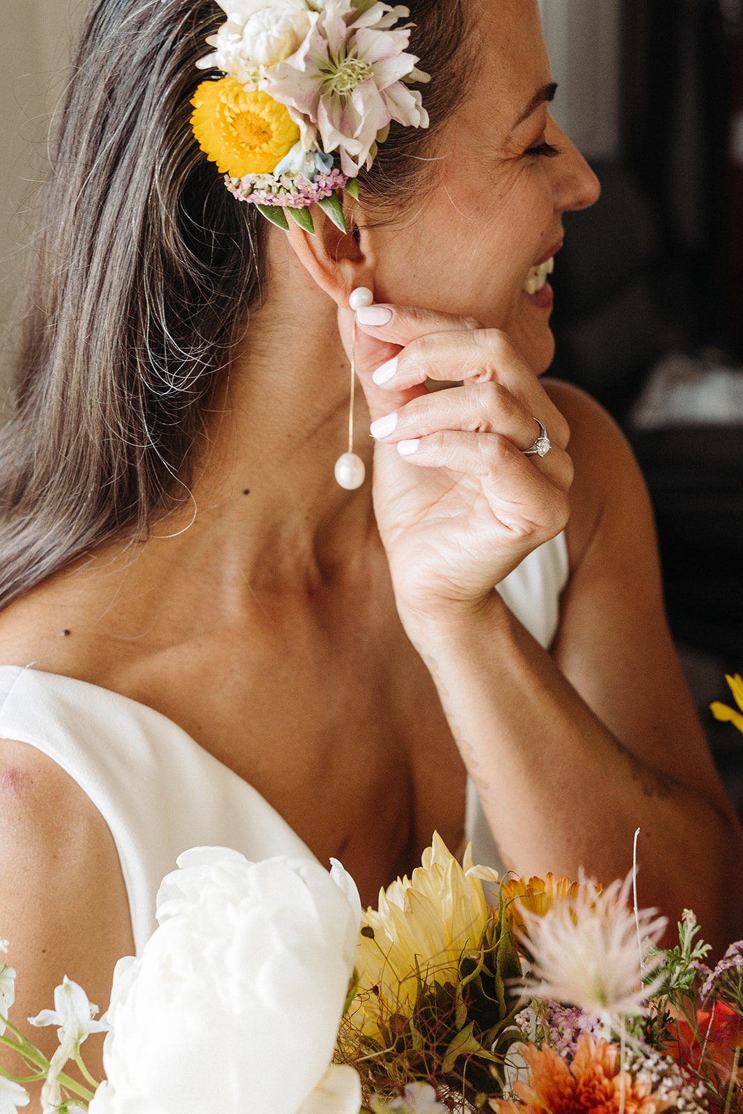 The bride touching her dangly pearl earring and the sun lights up her floral hair accent and large colorful bouquet.