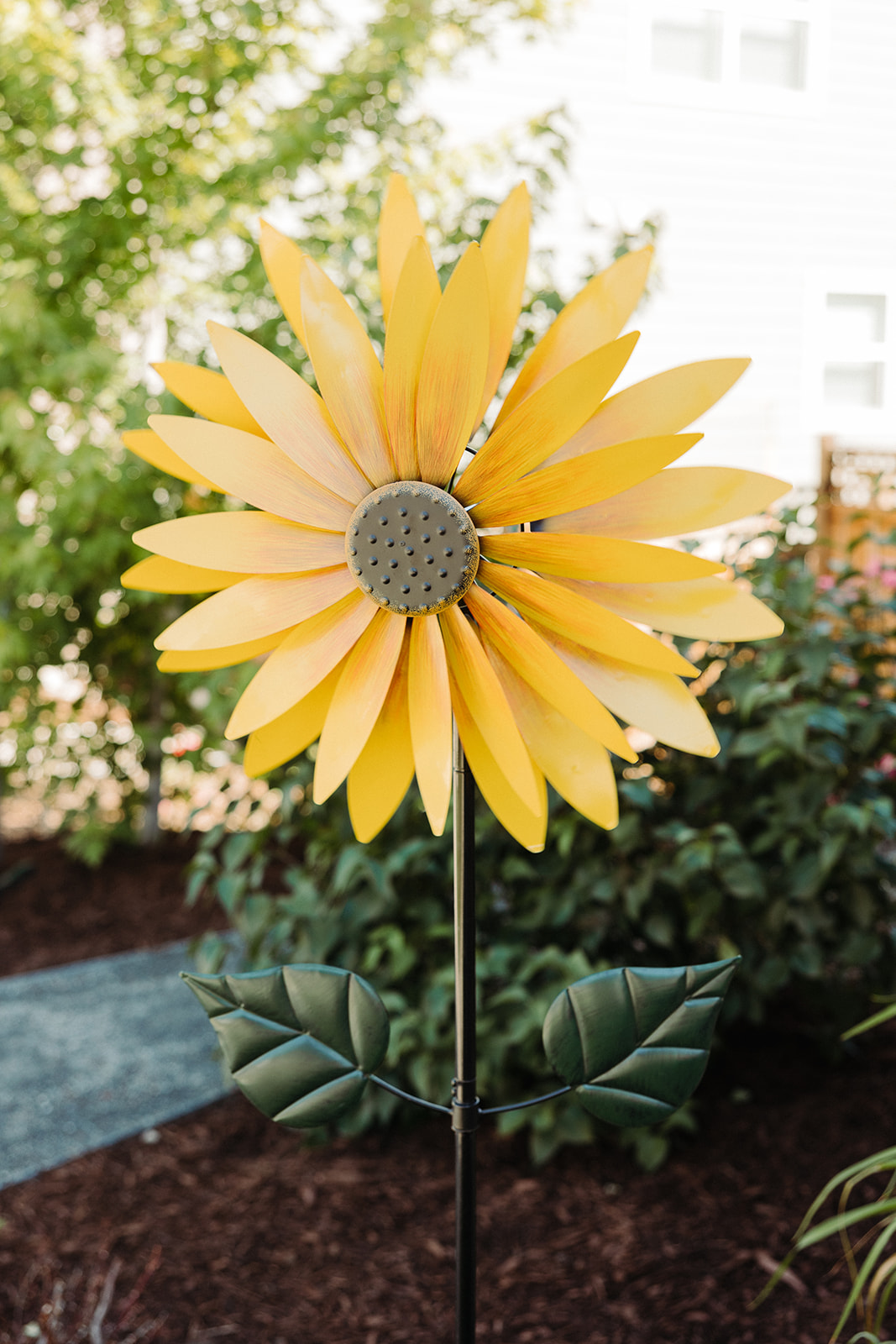 A metal sunflower that's petals blow in the wind; a bright yellow garden decoration on a sunny day.