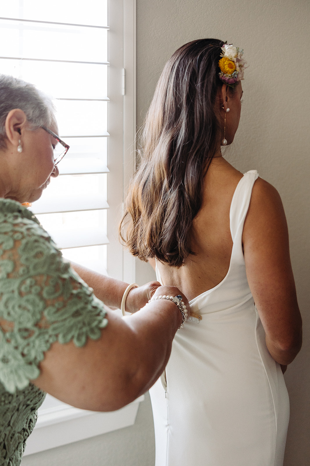 The mother of the bride helping her daughter zip up and fasten the timeless low-back gown.