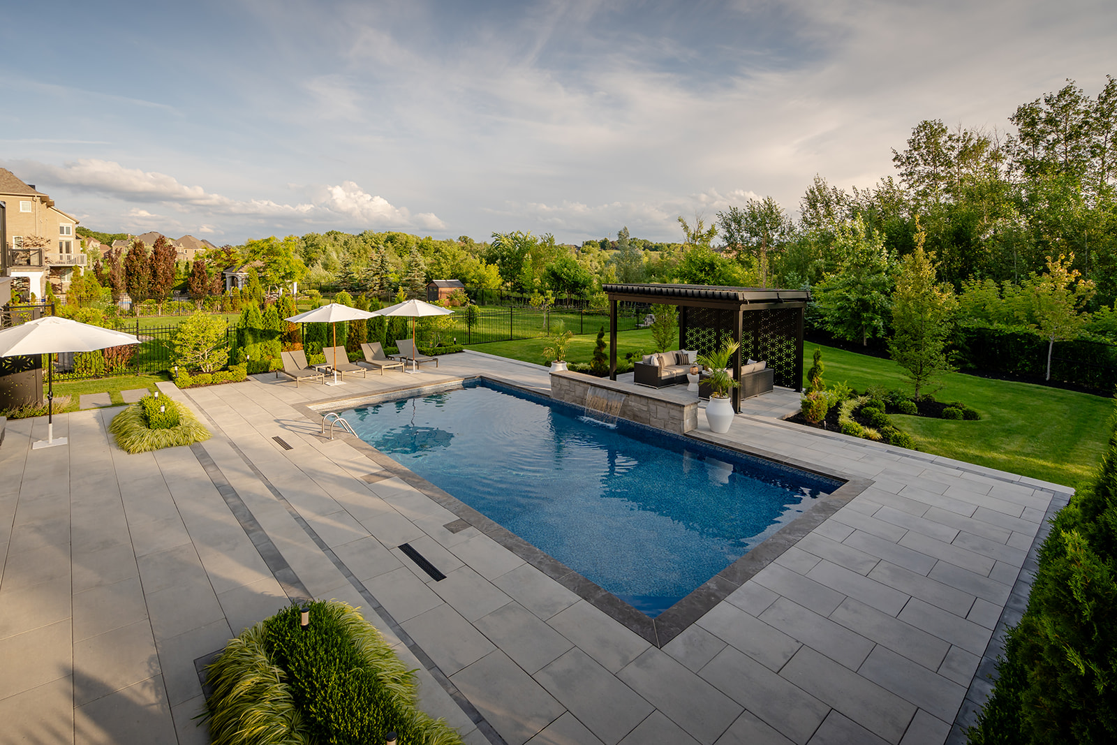 An inground pool with patio stones surrounding the pool, 3 open umbrellas and four lounge chairs.