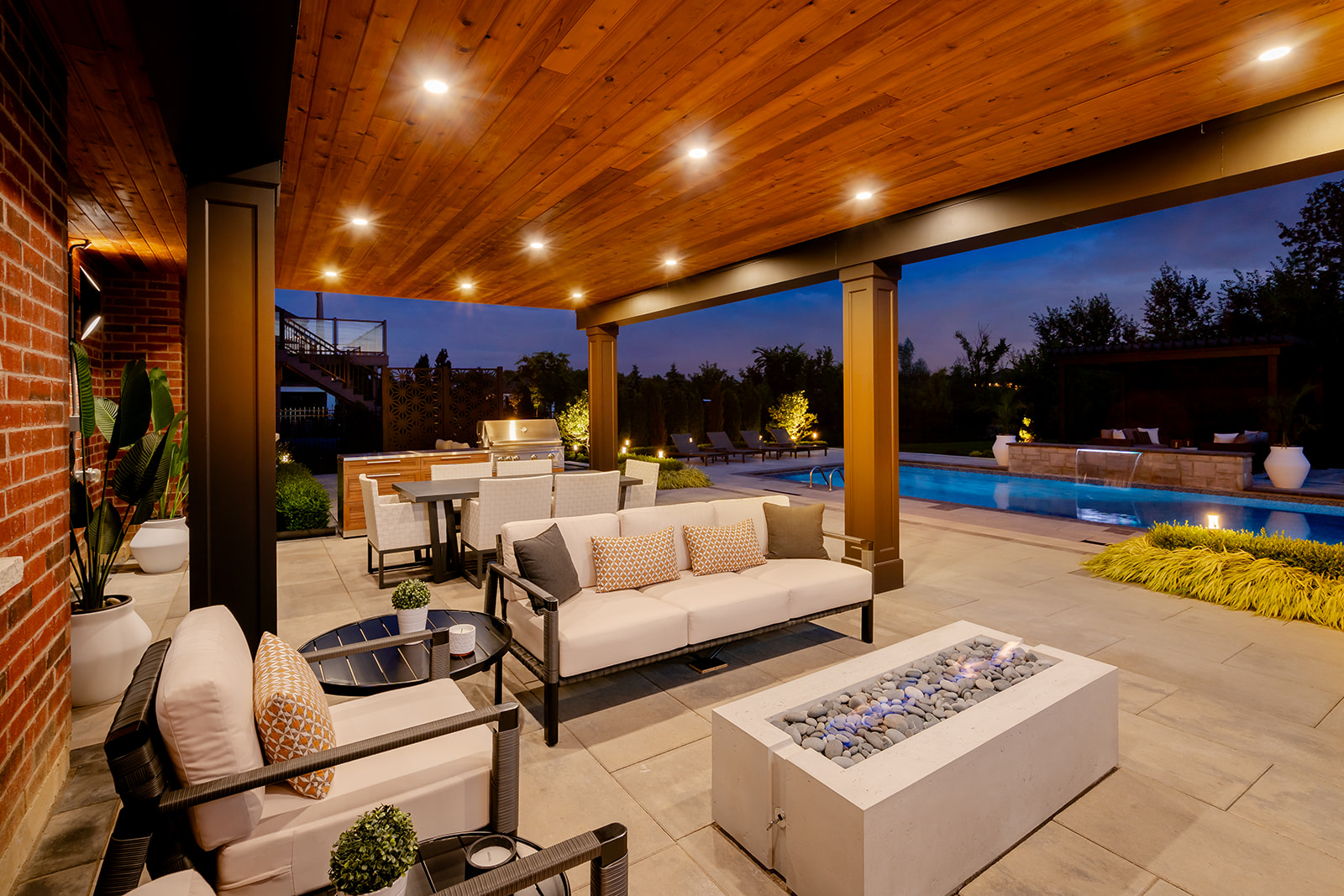 An outdoor patio set with a fireplace in the middle and lights turned on, on the cieling.