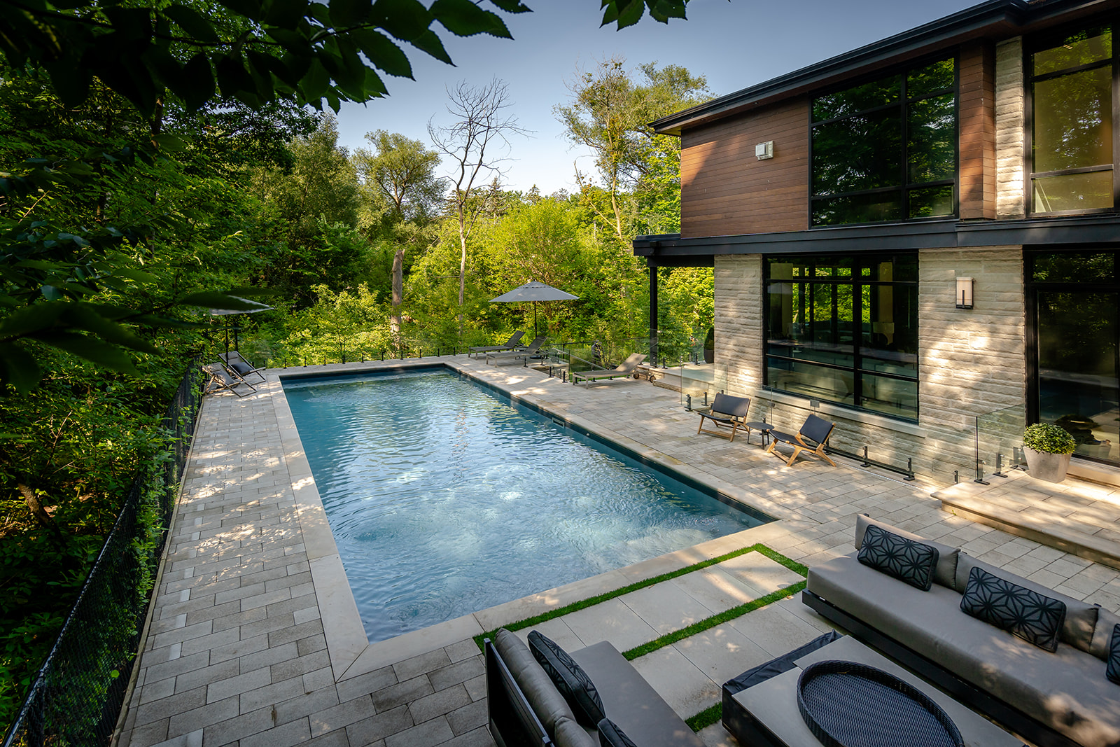 An inground pool with an outdoor patio set, two umbrellas open near the back and chairs scattered around the pool.