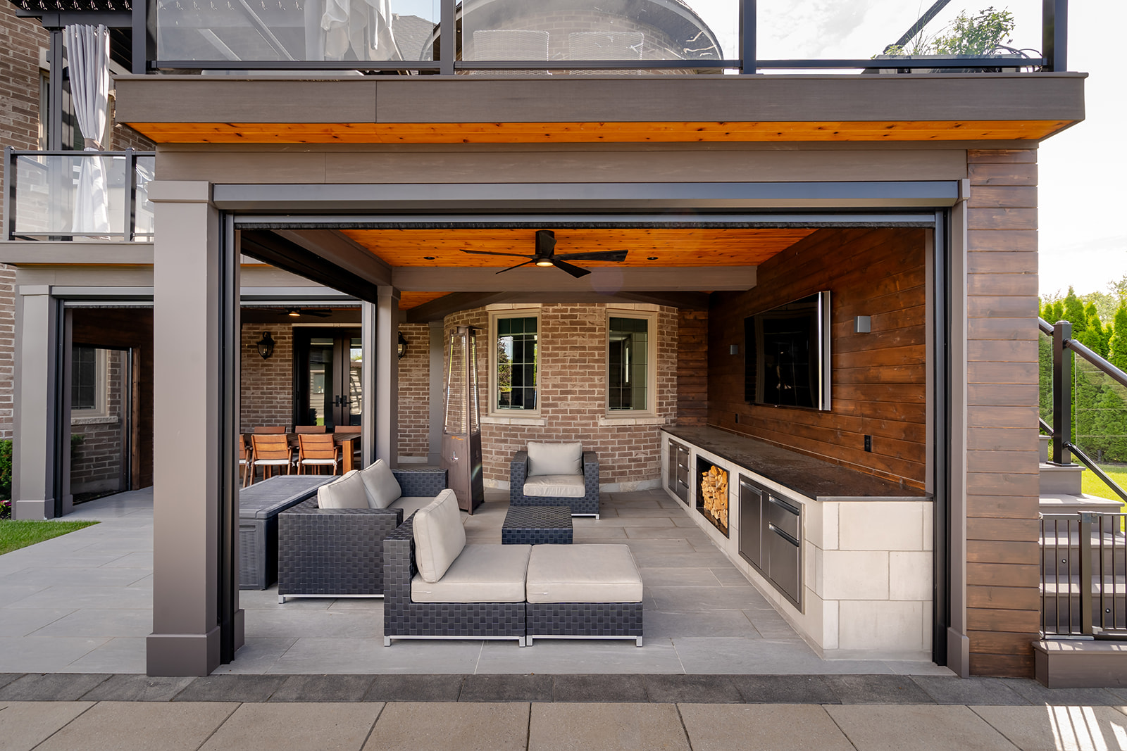 An outdoor patio set underneath a deck with a fan on the ceiling and an outdoor table on the left.