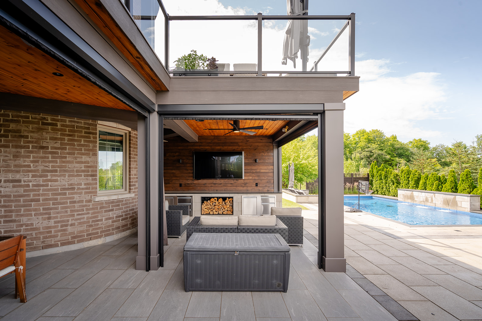 An outdoor patio set underneath a deck with an inground pool on the right.