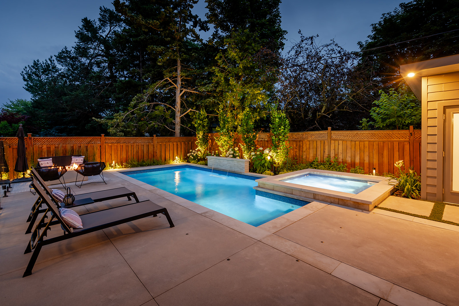 An inground pool with a jacuzzi and lights on.