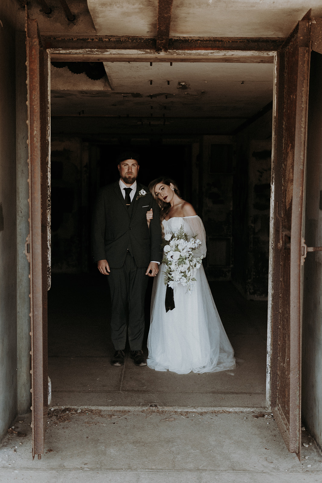 An eloping couple wearing a white wedding dress and a green suit posing in an abandoned building in Fort Worden.