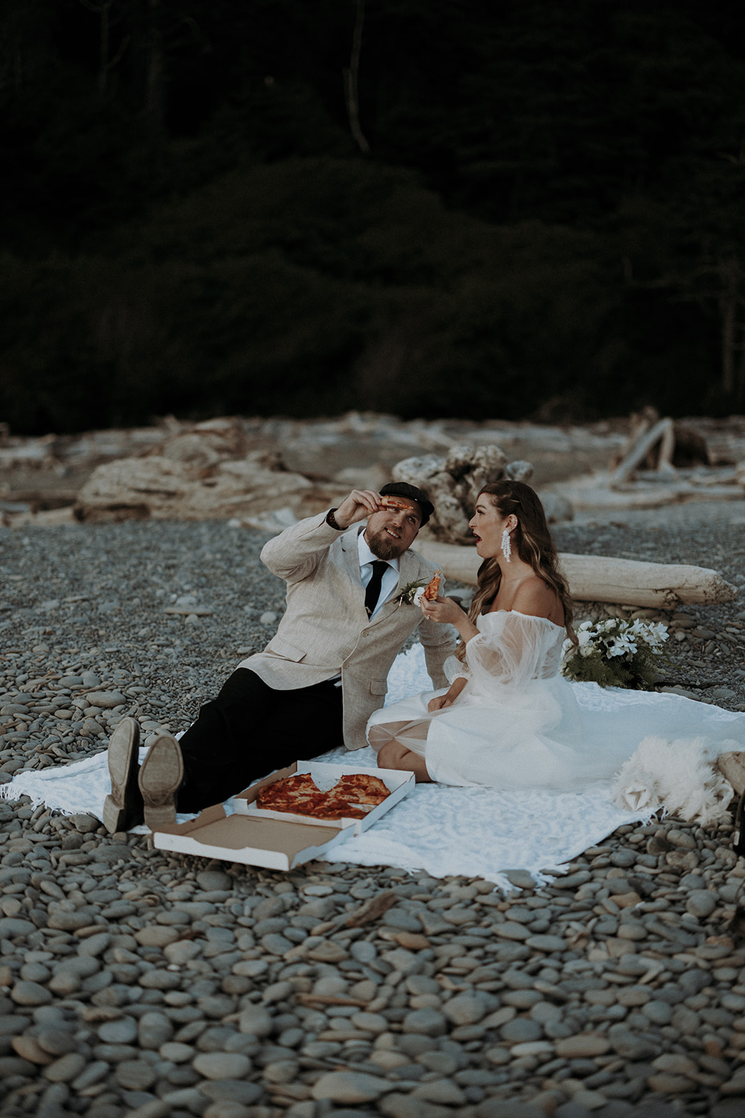 A couple eloping at Ruby Beach in Olympic National Park sitting down and having a pizza picnic.