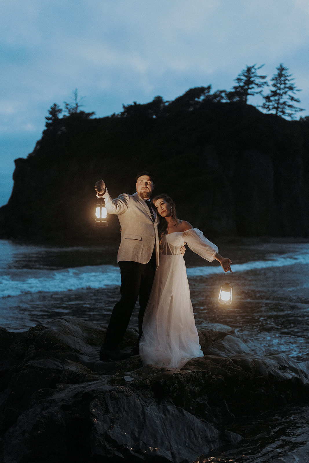 An eloping couple at Ruby Beach in Olympic National Park holding lanterns at night with a sea stack in the background.