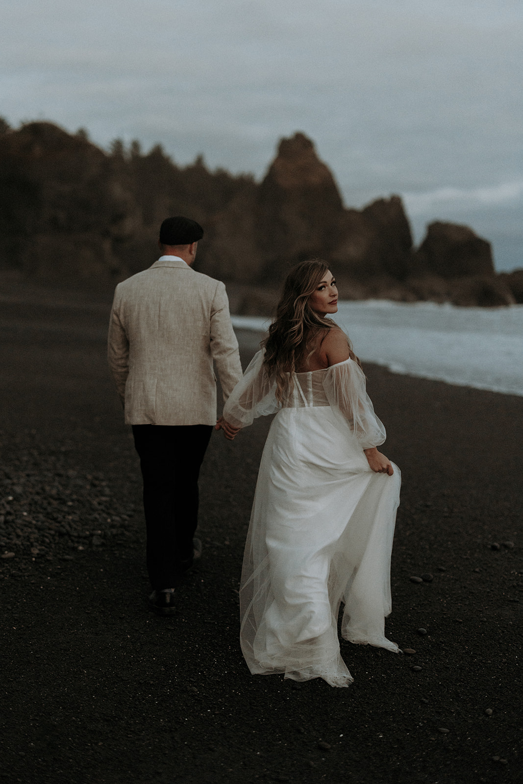 An eloping couple at Ruby Beach in Olympic National Park walking away with the bride looking back.