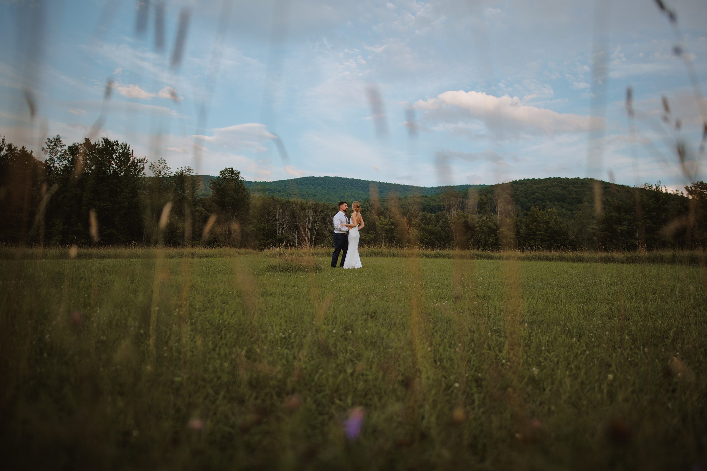 Just married couple stands in her uncle's field in the Catskills surrounded by overgrown grass and wildflowers