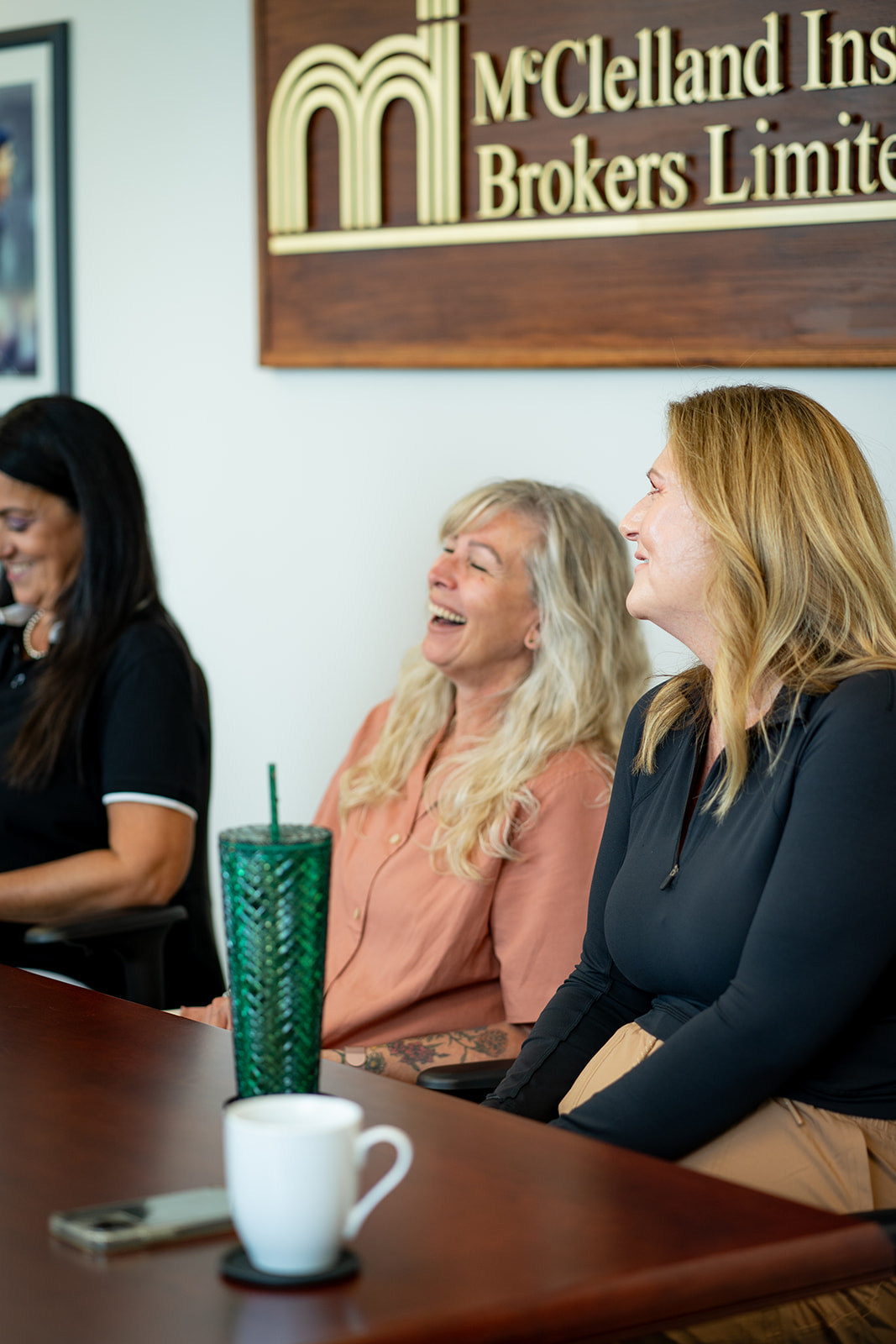 A lady laughing in a boardroom next to two other ladies.