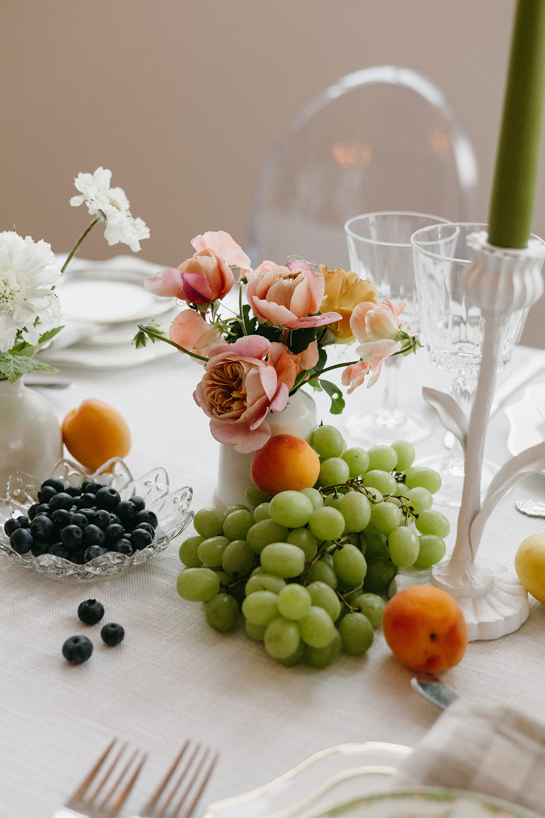 A dainty, soft pink floral arrangement surrounded by citrus fruit atop a garden party wedding tablescape. 