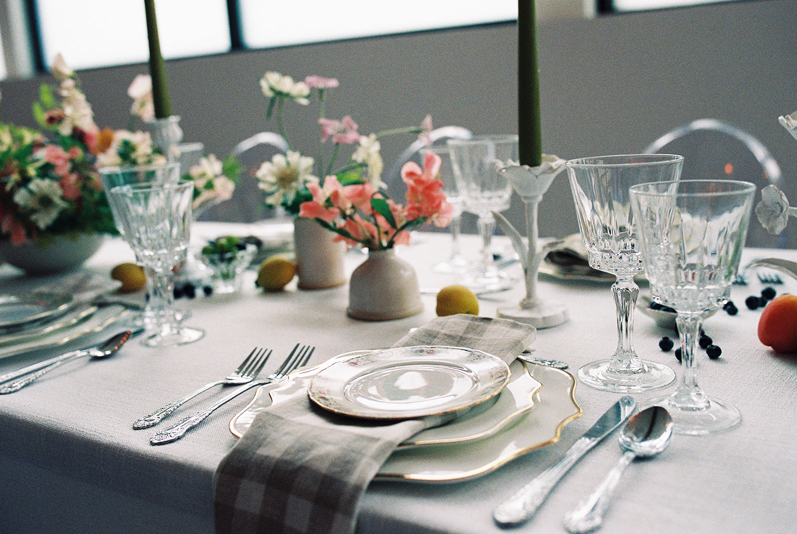 A garden party wedding tablescape featuring crystal glassware, bright florals, and vintage place settings on film.