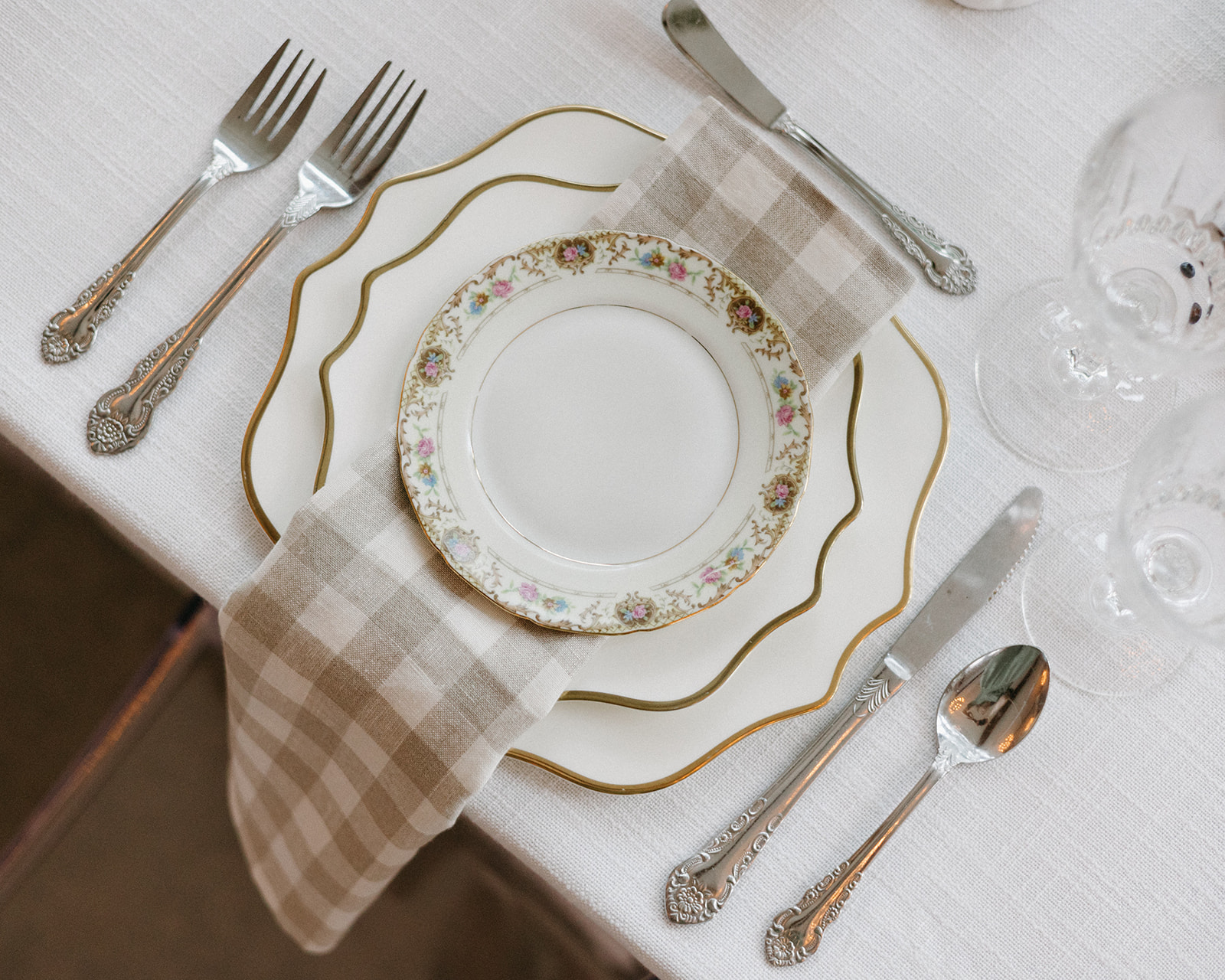 A garden party wedding tablescape featuring a vintage plate setting, gingham napkin, and silver flatware on film.  