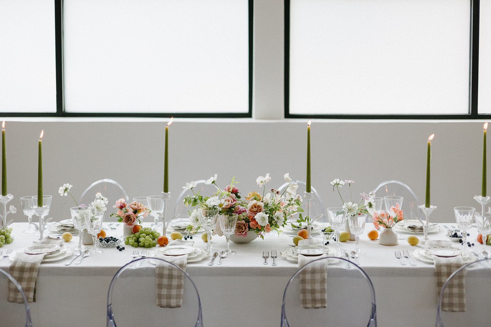 A garden party wedding tablescape featuring lit, green taper candles, bright florals, and vintage place settings. 