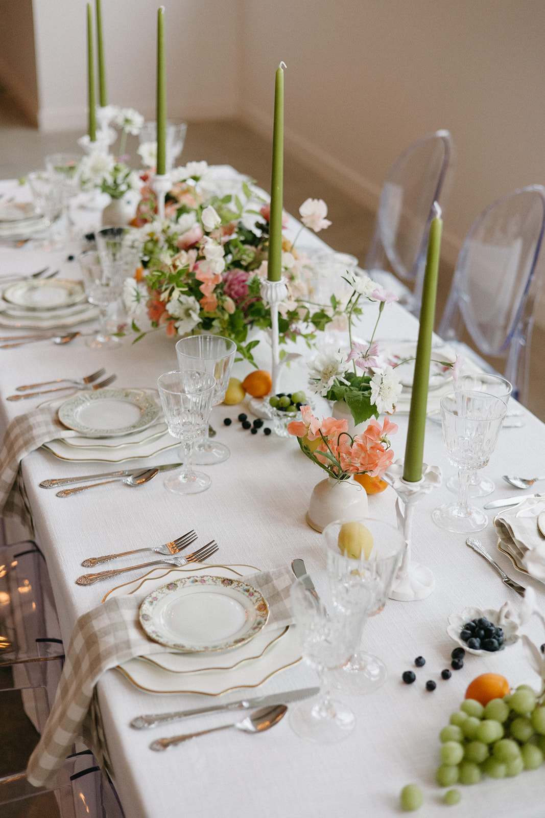 A garden party wedding tablescape with bright florals, vintage place settings, fruit, and green taper candles. 