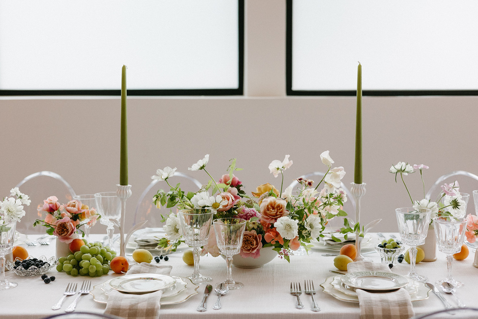 A springtime tablescape with bright florals, green taper candles, vintage plate settings, gingham napkins, and fruit. 