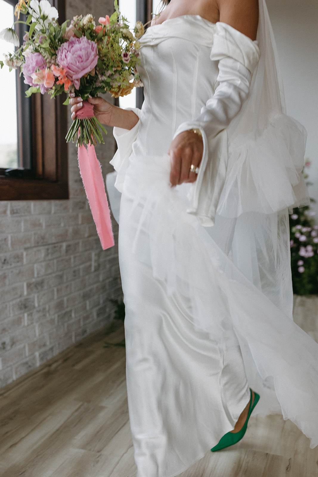 An elegant bride in a long, white wedding dress holds a bright, floral garden party wedding bouquet by Figment Floral.