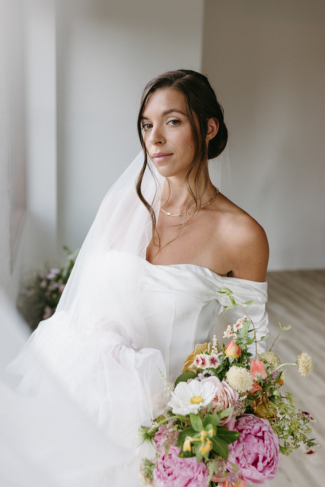 A elegant wedding portrait of a woman holding a bright bridal bouquet, wearing an off-the-shoulder wedding gown and veil