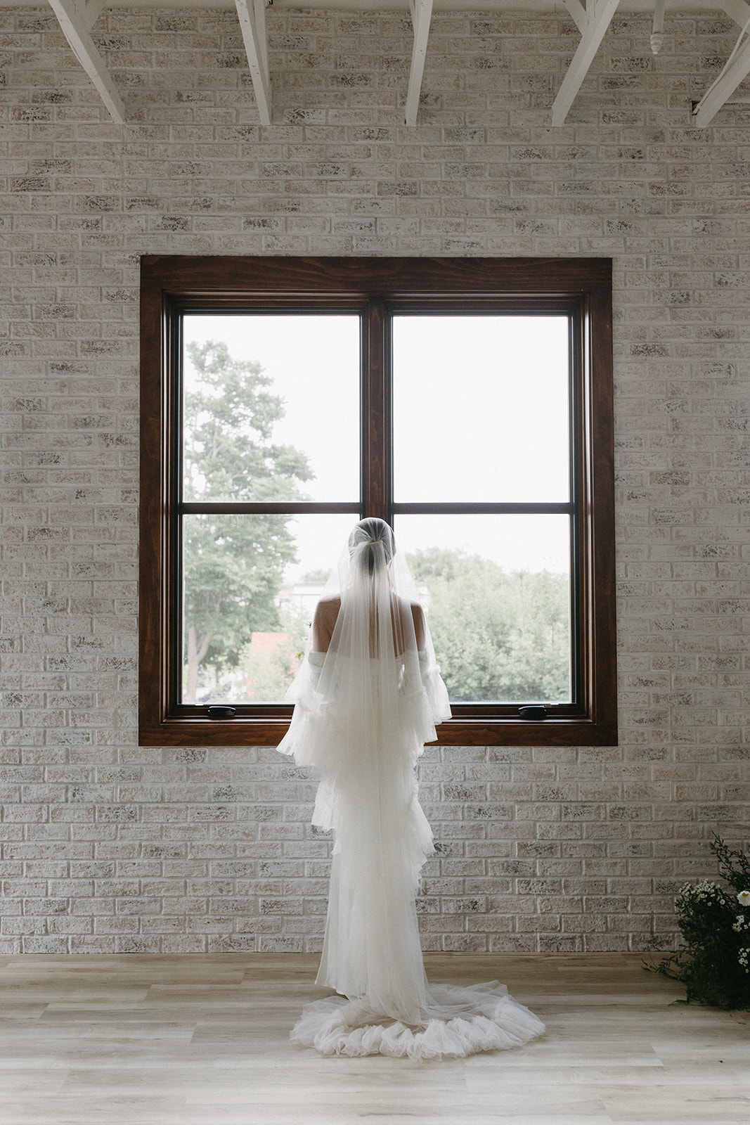 A bride looks out a glass window wearing a sophisticated wedding dress at a garden party wedding ceremony at The Simon. 