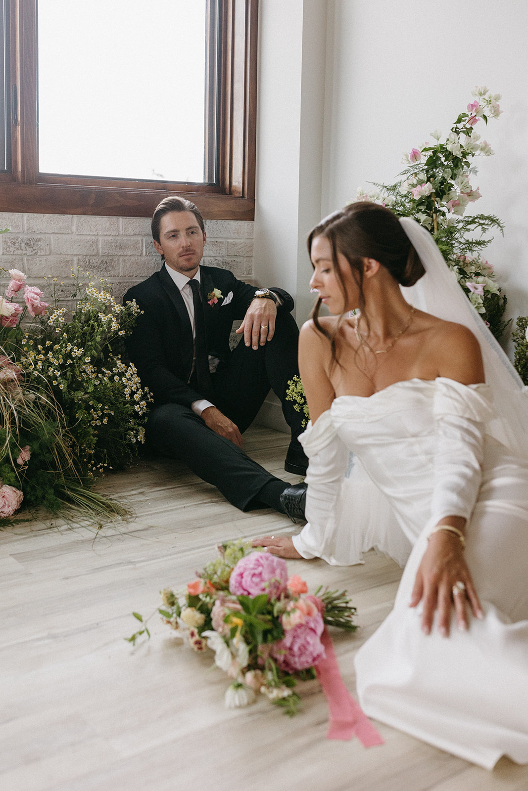 An elegant bride and groom sit on the floor of The Simon, surrounded by garden party wedding floral arrangements.