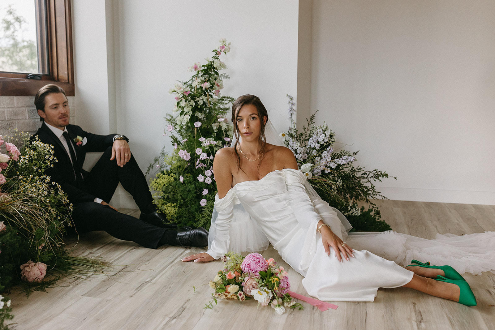 A garden party wedding bride and groom sit on the floor of The Simon surrounded by wedding floral by Figment Floral. 