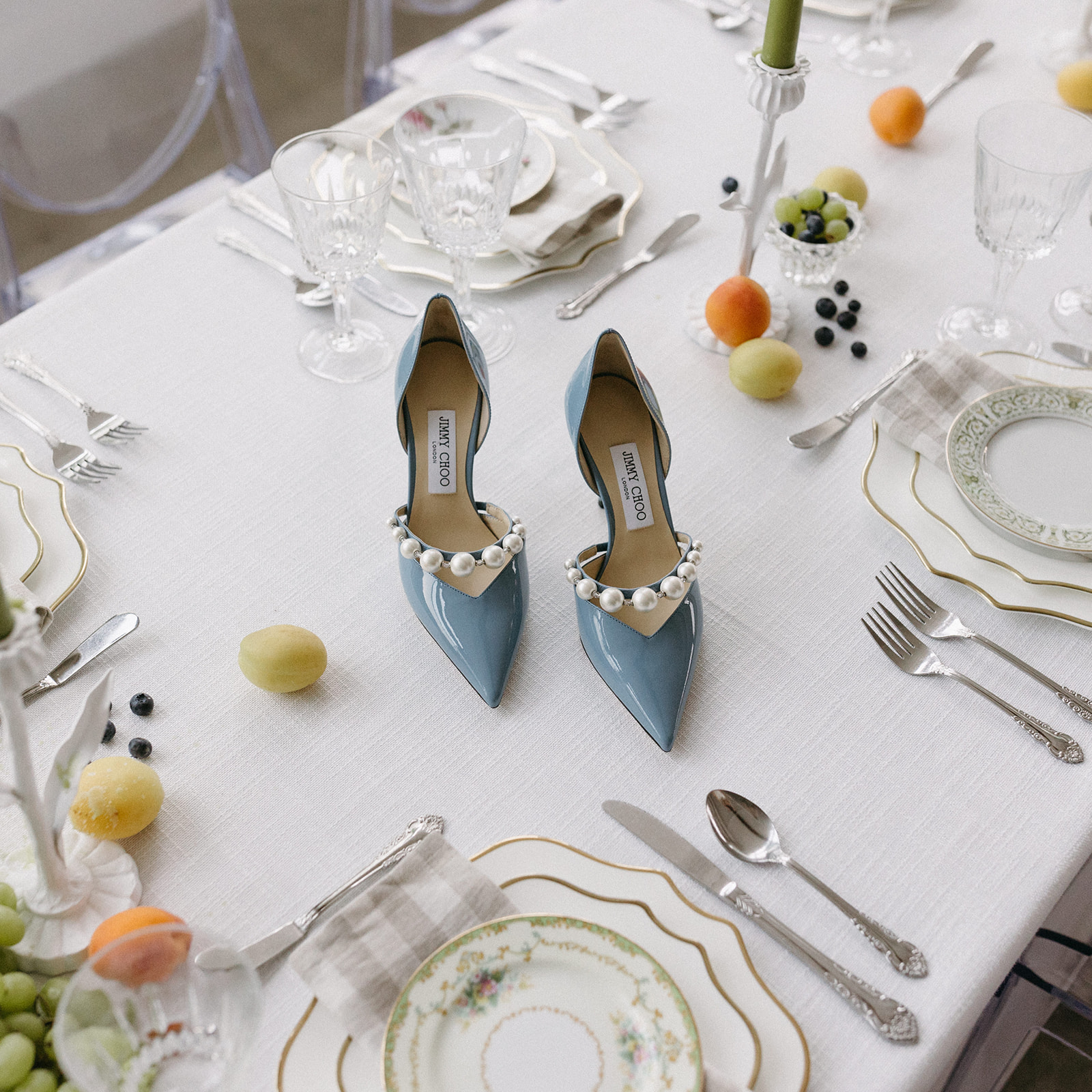 A styled garden party wedding tablescape featuring a linen tablecloth, citrus fruit, blue Jimmy Choo heels, and 