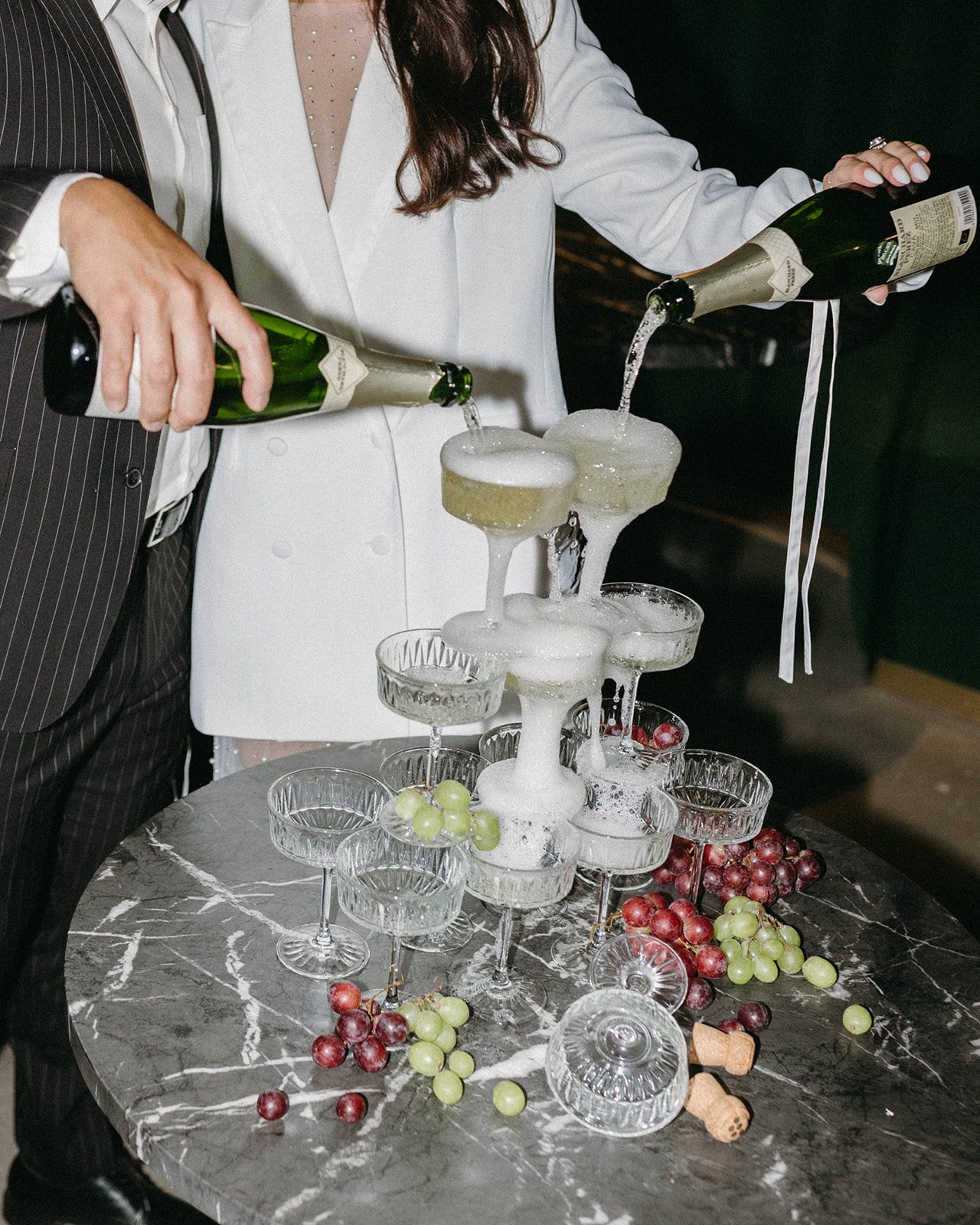 A bride and groom at a speakeasy wedding pour champagne into a champagne glass tower at The Simon. 