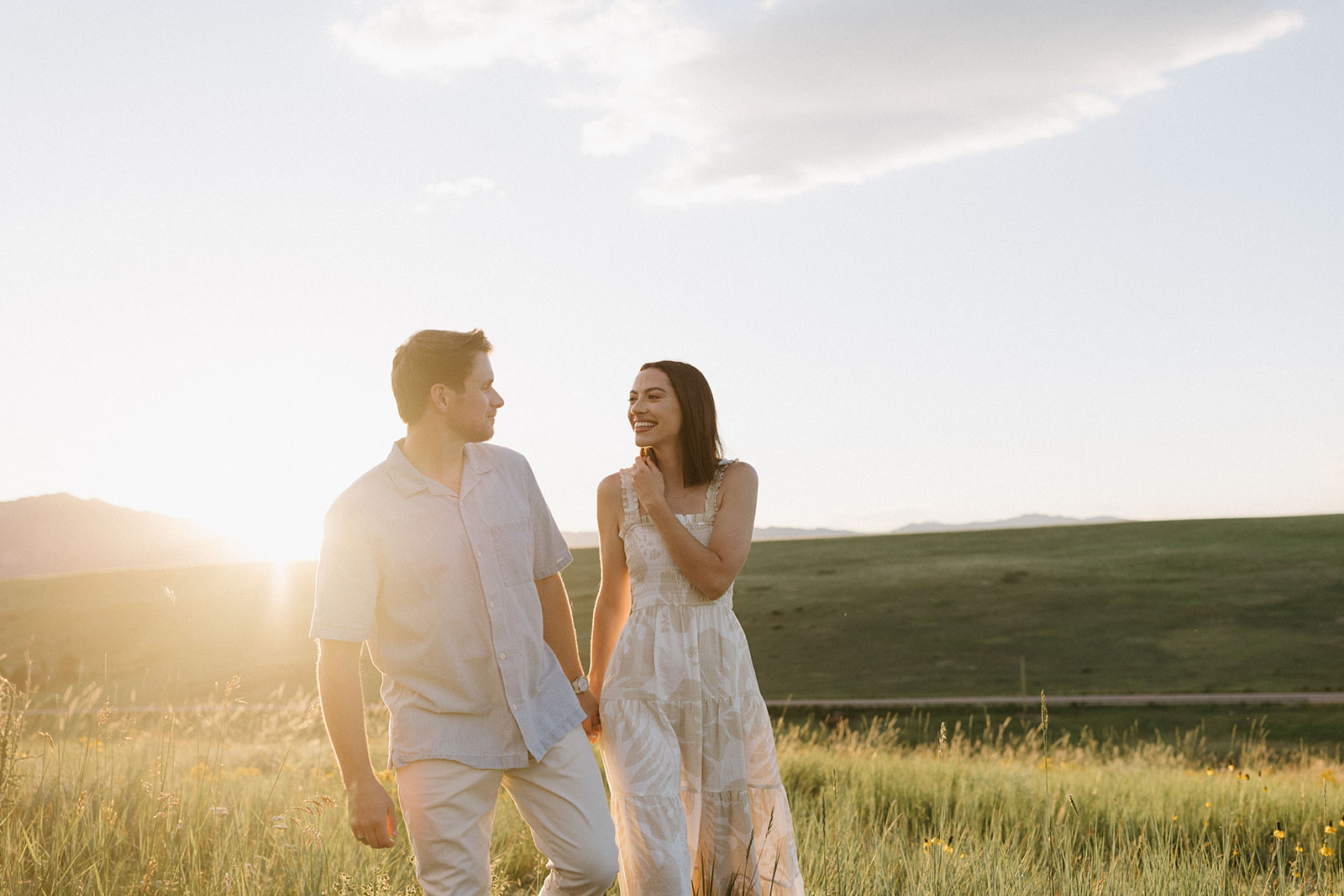 A modern, fashion-forward engagement couple holds hands while walking in a wildflower field in Colorado at Sunset. 