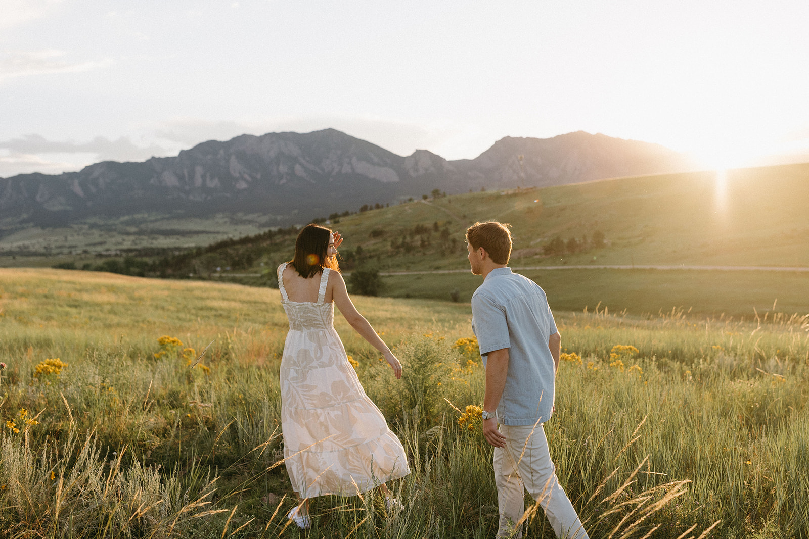 A scenic view of Boulder's Flatirons with a couple in neutral-toned attire, surrounded by a blooming wildflower meadow.