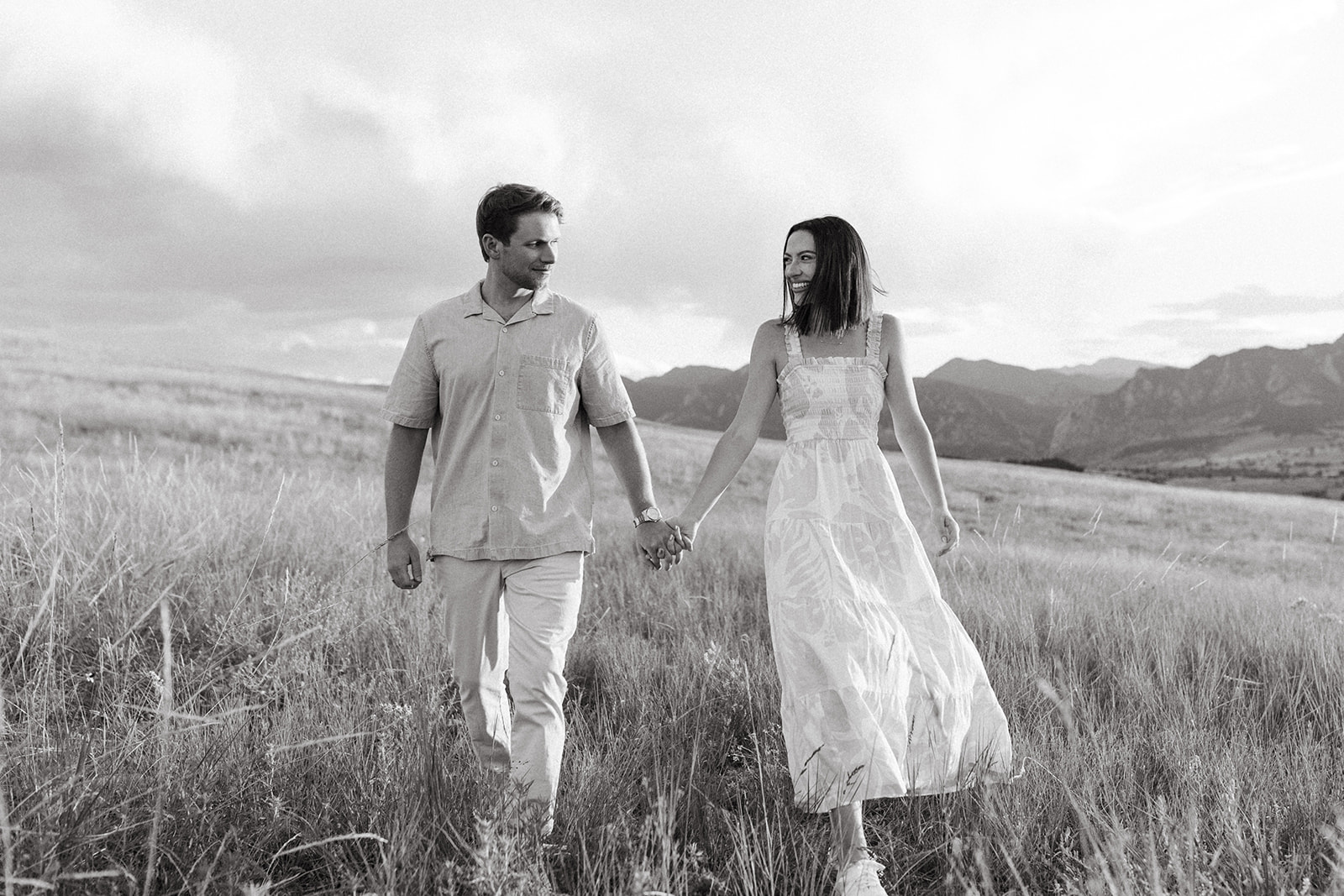 An engaged couple holds hands while walking in a wildflower meadow during a Colorado engagement session in Boulder