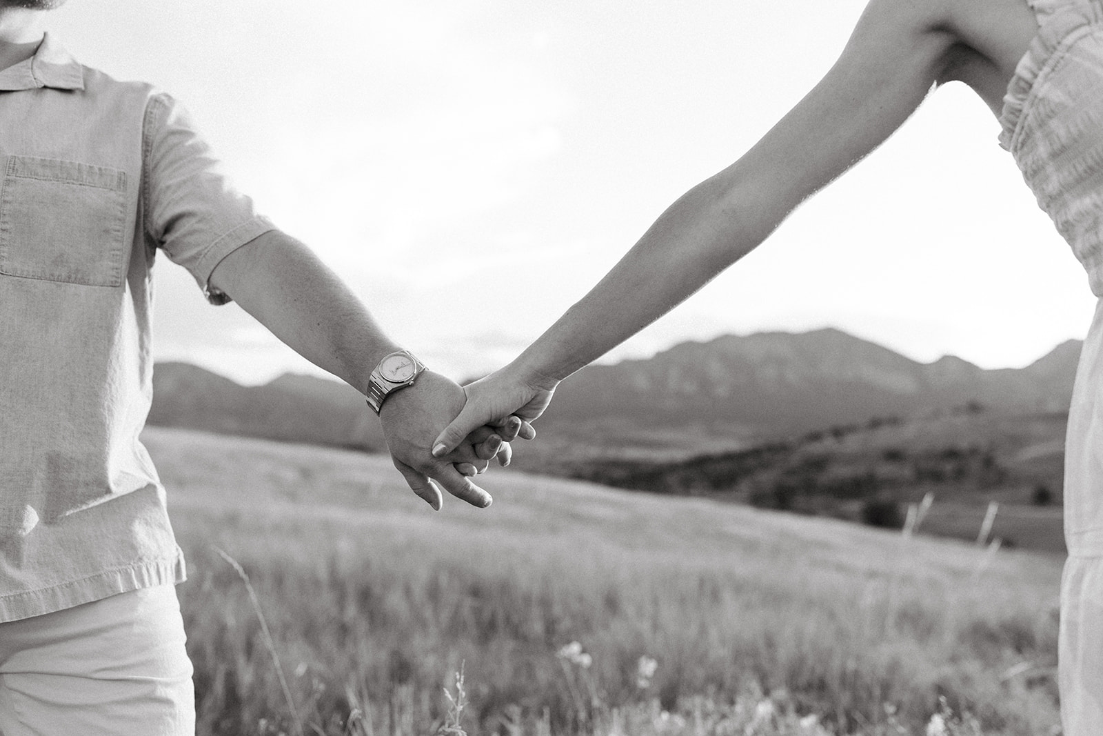 An editorial engagement couple holds hands in a wildflower meadow near The Flatirons in Boulder, Colorado