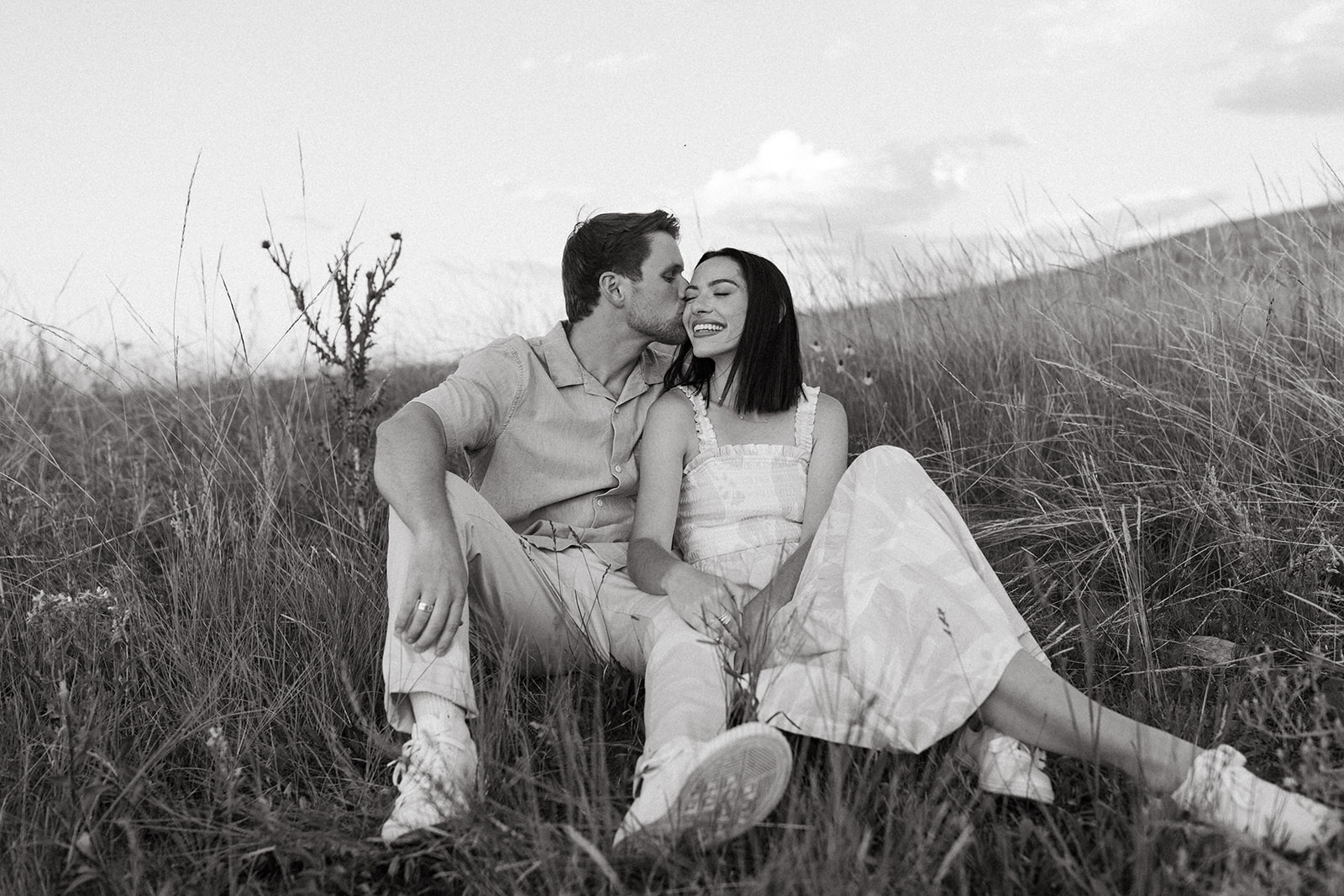 An editorial engagement couple in neutral attire sits among  wildflowers during a Sunset couples session in Boulder
