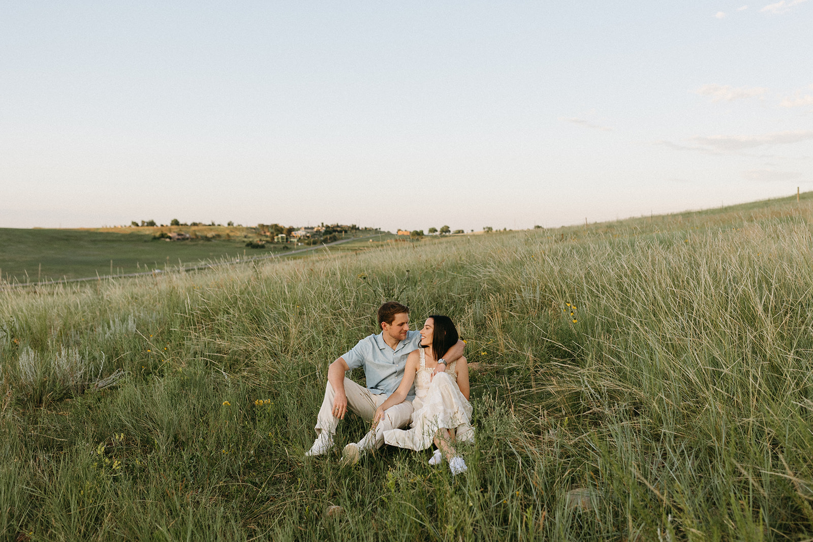 An editorial engagement couple in neutral attire sits among colorful wildflowers during a colorful Sunset in Boulder