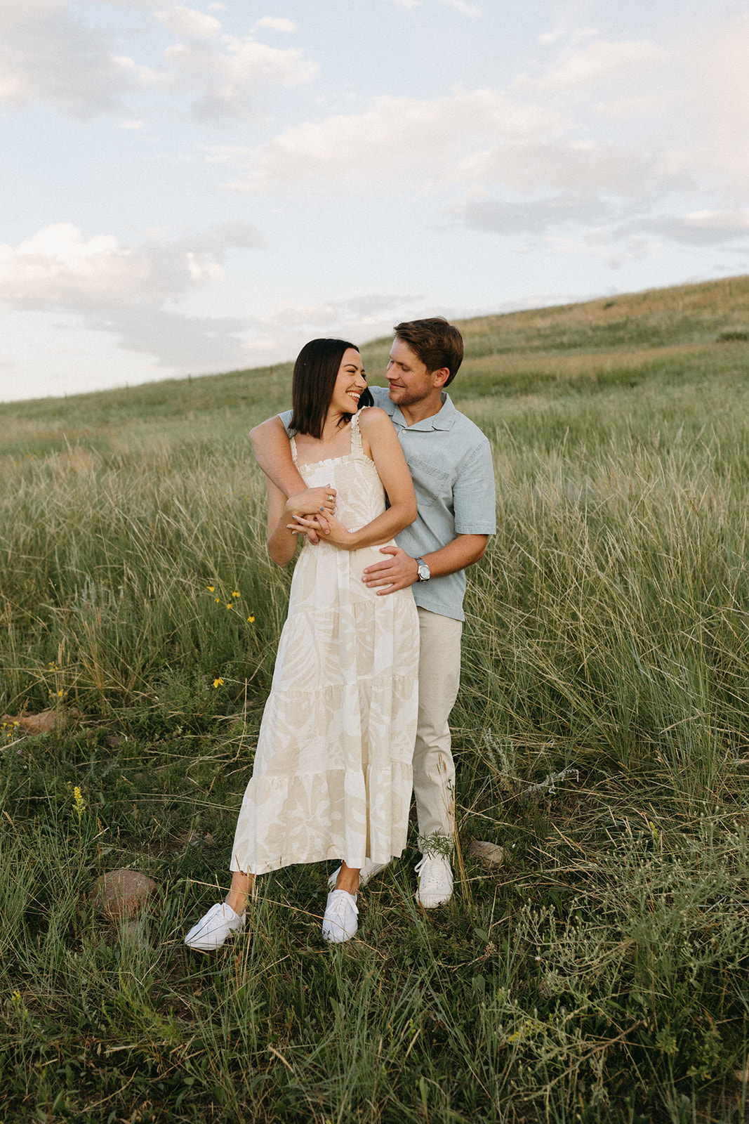 A couple in neutral attire embraces while surrounded by colorful wildflowers in a meadow in Boulder, Colorado
