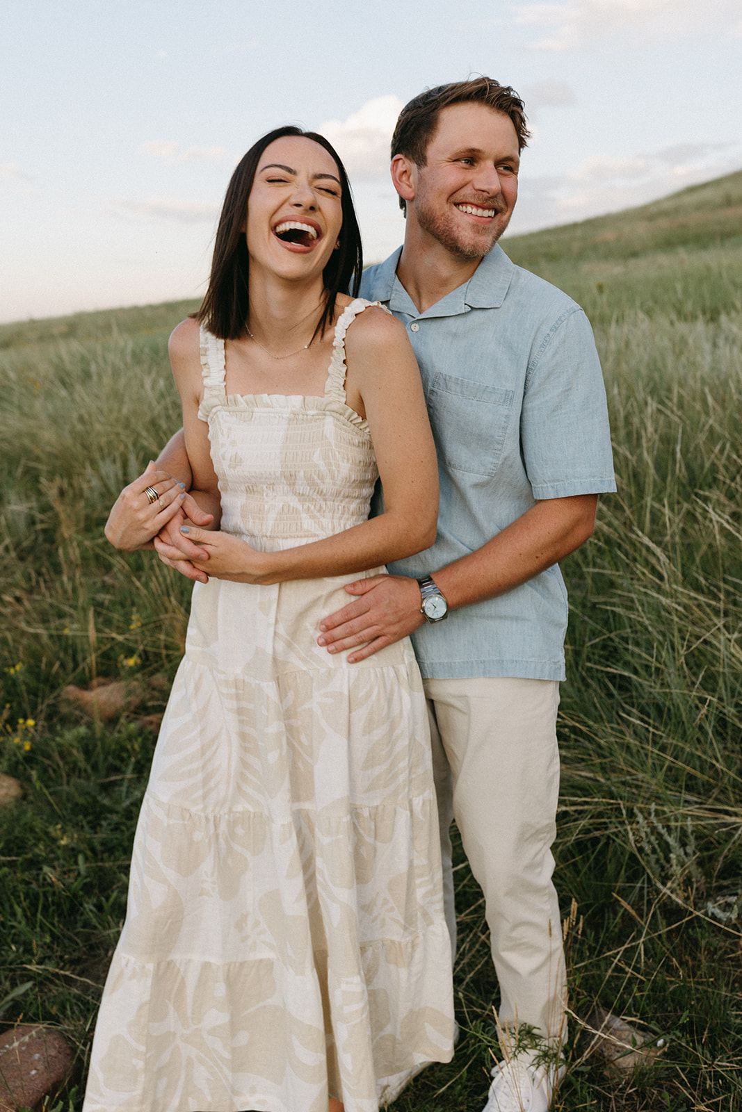 A couple in neutral attire shares a laugh together, surrounded by a colorful wildflower meadow in Boulder, Colorado