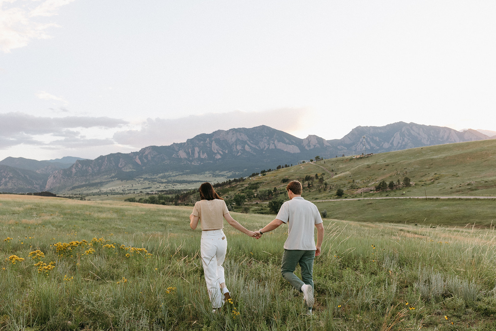 A man and fiancée hold hands in a wildflower meadow during an engagement session near The Flatirons in Boulder, Colorado