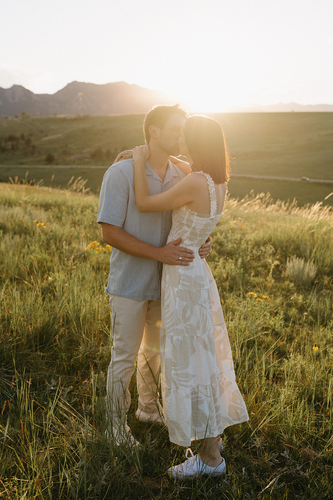 An editorial engagement couple kiss and embrace at Sunset in a wildflower meadow in Boulder, Colorado