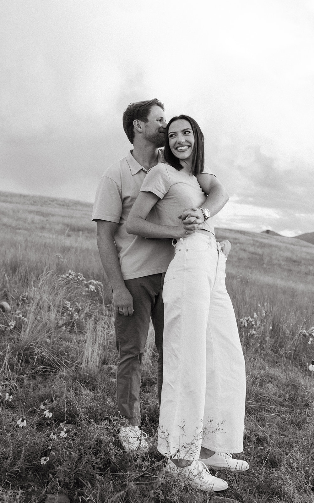 A modern, fashion-forward engagement couple embraces while smiling for a portrait in a wildflower meadow in Colorado