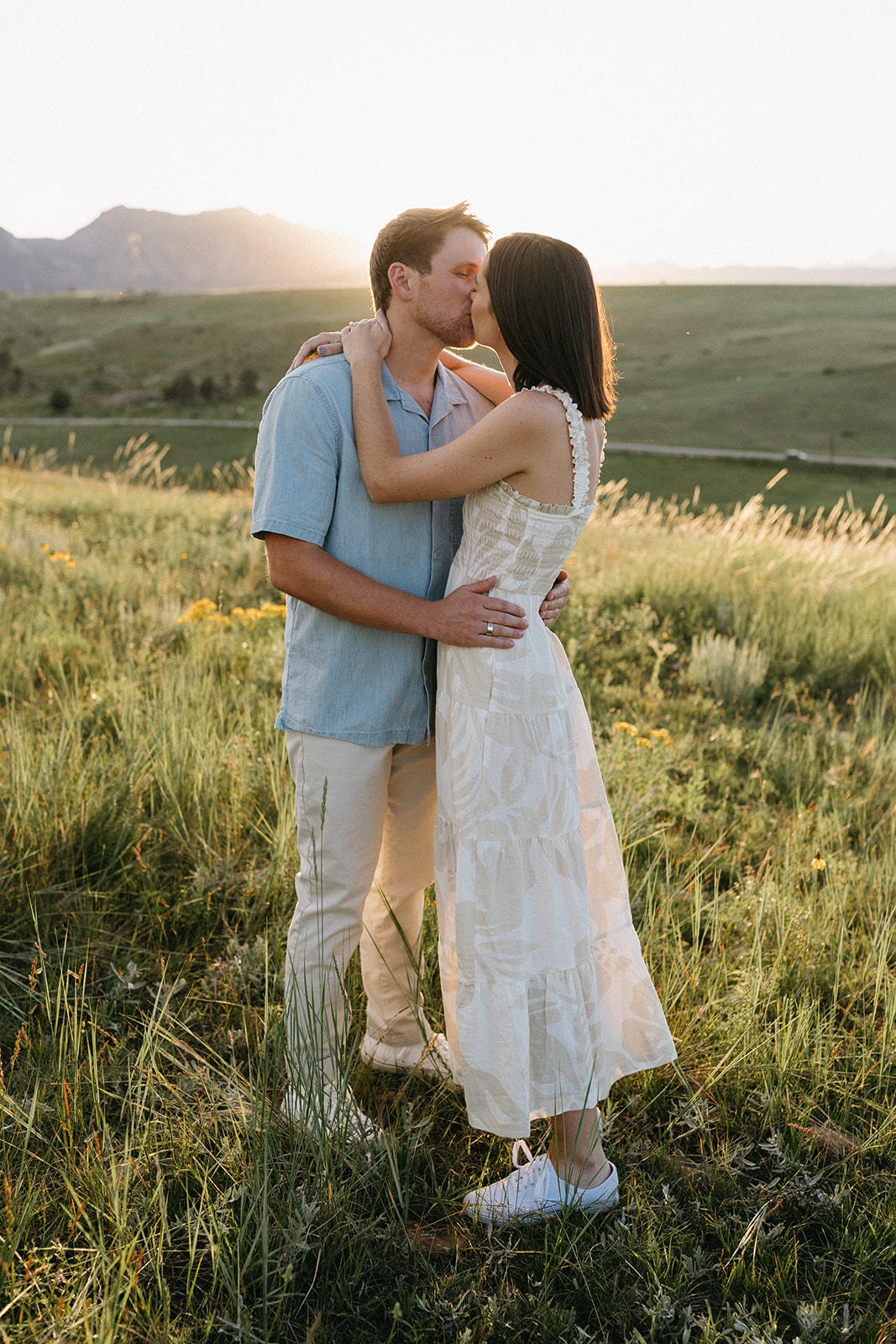 An editorial engagement couple kiss and embrace at Sunset in a wildflower meadow near The Flatirons in Boulder, Colorado
