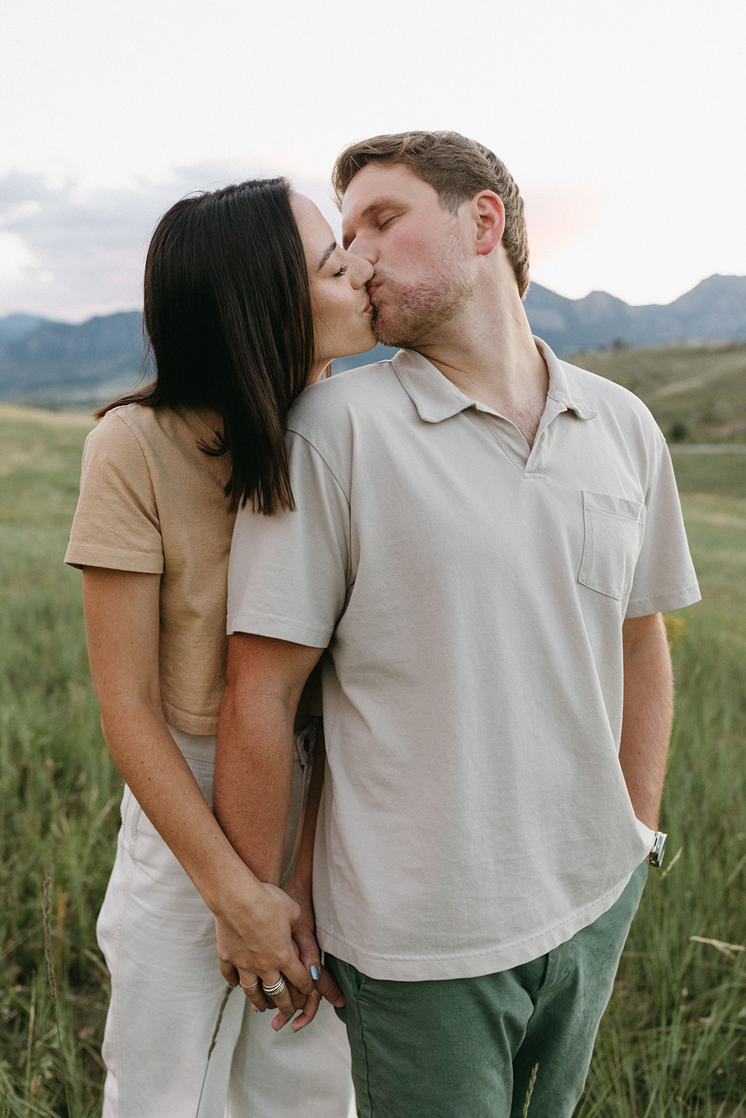 An editorial engagement session couple wearing natural-tone outfit kisses in a wildflower meadow near in Colorado