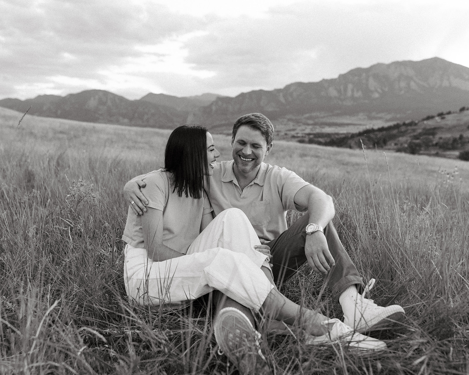 A stylish engaged couple sits in a stunning wildflower meadow, with Boulder's Flatirons in the background